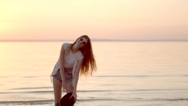 Mooie vrouw in hoed en zonnebril poseren achtergrond van Oceaan en gouden zonsondergang — Stockvideo