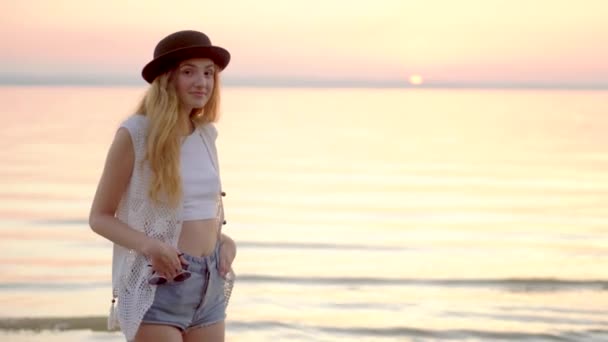 Linda joven con sombrero posando en el fondo del océano y la puesta de sol de oro — Vídeos de Stock