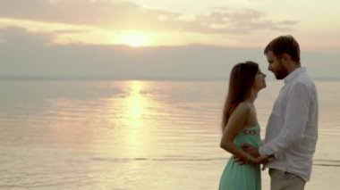 Mutlu genç çift sahilde günbatımı üzerinde. Onlar birbirlerinin bakıyorsun.