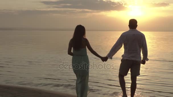 Unga lyckliga paret promenerar på stranden på solnedgången. Begreppet kärlek. — Stockvideo