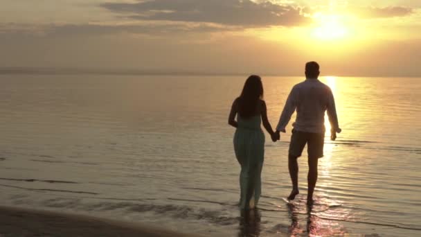 Joven pareja feliz caminando por la playa al atardecer. Concepto de amor . — Vídeos de Stock