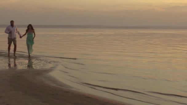 Ευτυχισμένο ζευγάρι τρέχει στην παραλία το ηλιοβασίλεμα. Έννοια της αγάπης. — Αρχείο Βίντεο