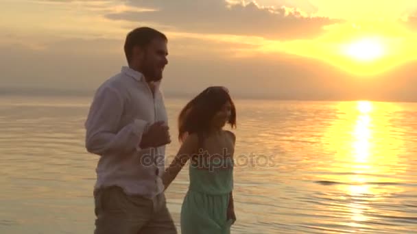 Joven pareja feliz corriendo en la playa al atardecer. Concepto de amor . — Vídeos de Stock