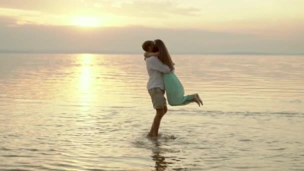 Jovem homem feliz pegar e rodopiar sua namorada na praia ao pôr do sol . — Vídeo de Stock
