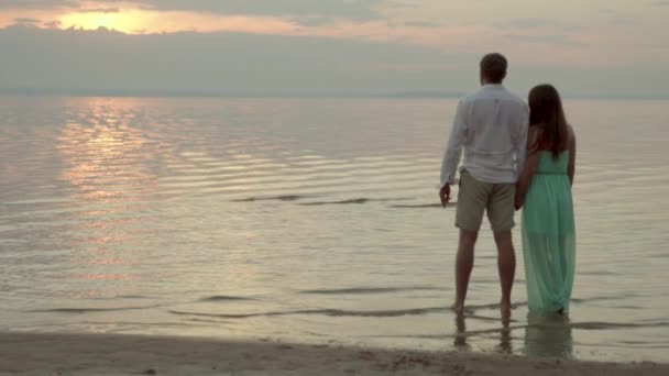 Feliz jovem casal olhar para o mar no pôr do sol conceito de amor e relacionamentos — Vídeo de Stock