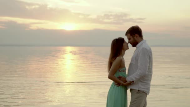 Щаслива молода пара на пляжі на заході сонця. Вони дивляться одне одному в очі . — стокове відео