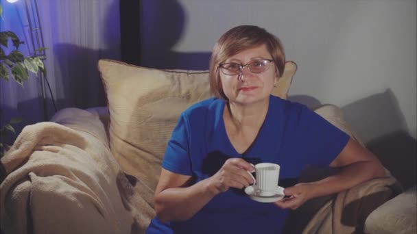 Mulher idosa feliz sorrindo, sentada na poltrona bebendo chá — Vídeo de Stock