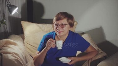 Gülümseyerek, çay içme koltukta oturan mutlu yaşlı kadın