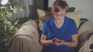 Yaşlı kadın evde akıllı telefon kullanarak koltukta oturan