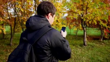 Onun smartphone kullanarak sonbahar Park'ta yürüyordunuz siyah ceketli genç adam