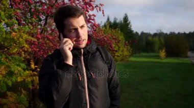 Sonbahar park ağır çekimde telefonda konuşurken siyah ceketli genç adam