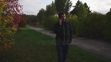 Yürüyüş ve sonbahar parkta telefonda konuşurken siyah ceketli genç adam