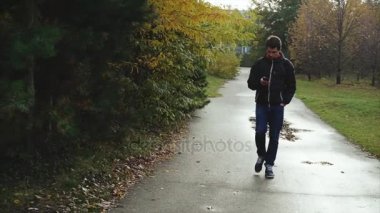 Onun smartphone kullanarak sonbahar Park'ta yürüyordunuz siyah ceketli genç adam