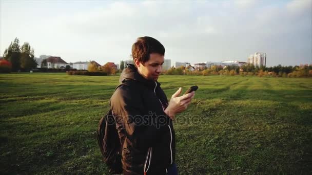 Jovem de casaco preto navegar na internet usando seu smartphone ao ar livre — Vídeo de Stock