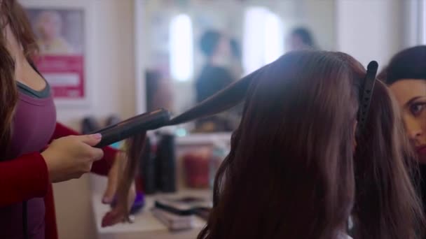 Κομμωτήριο κάνοντας κόμμωση με σίδερο μαλλιών ενώ καλλιτέχνης μακιγιάζ εφαρμογή σκιές ματιών — Αρχείο Βίντεο