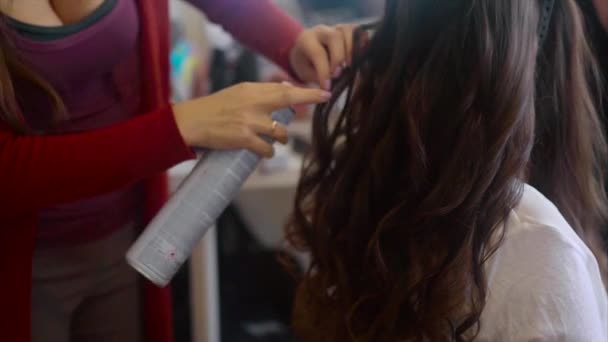 Close up shot of hairdresser sprays hairspray on brunette while making hair-do — Stock Video