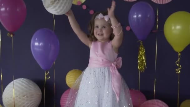Досить маленька дівчинка сміється і грає з повітряною кулею на її день народження — стокове відео