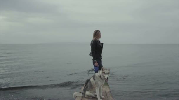 Молода приваблива жінка з сестринським хаскі собакою стоїть на узбережжі моря — стокове відео