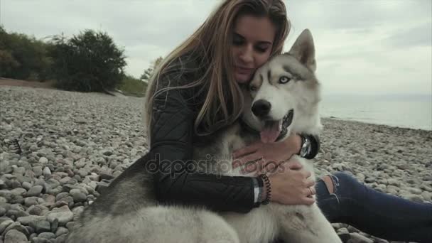 Mladá atraktivní dívka s sibiřský husky pes sedí na pobřeží — Stock video