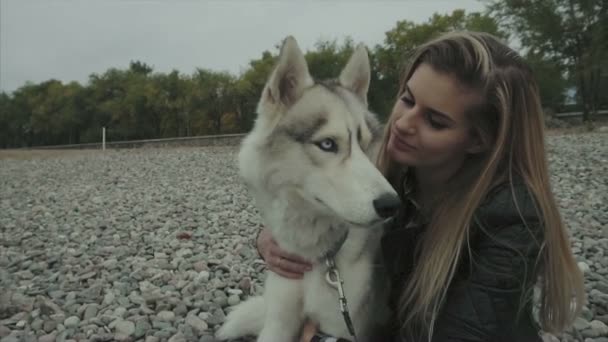 Jovem mulher bonito com siberiano husky cão sentado na costa — Vídeo de Stock