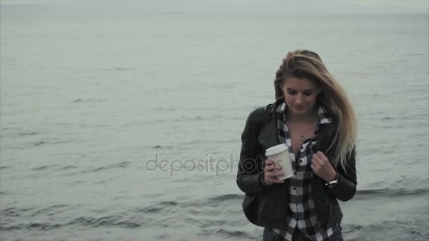 Attractive young blond woman holding a cup of coffee in her hands near the sea — Stock Video