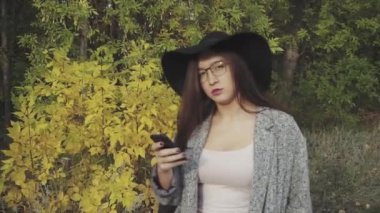 Genç güzel kadın siyah şapka ve gözlük onun smartphone açık kullanma