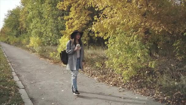 Молодая красивая женщина в черной шляпе идет по осенней улице — стоковое видео