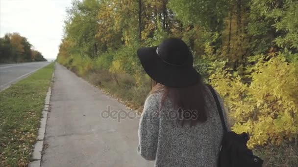 Jovem mulher bonita em chapéu preto e óculos andando pela rua de outono — Vídeo de Stock