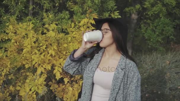 Mujer linda joven en sombrero negro y vasos de beber café al aire libre — Vídeos de Stock