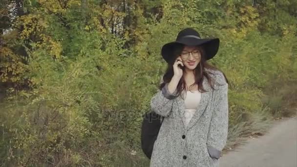 Jeune jolie femme en chapeau noir et lunettes appelant à son petit ami en plein air — Video