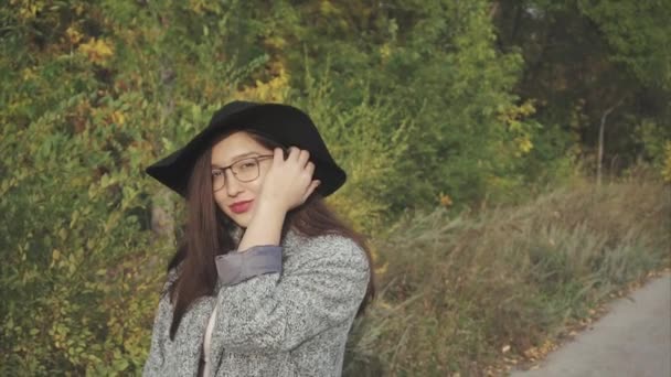 Ritratto di giovane bella donna sorridente in cappello nero e occhiali sulla strada autunnale — Video Stock