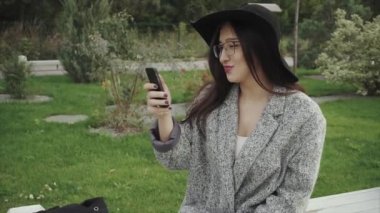 Genç çekici kadın parkta bankta oturur ve akıllı telefon üzerinde çalışıyor