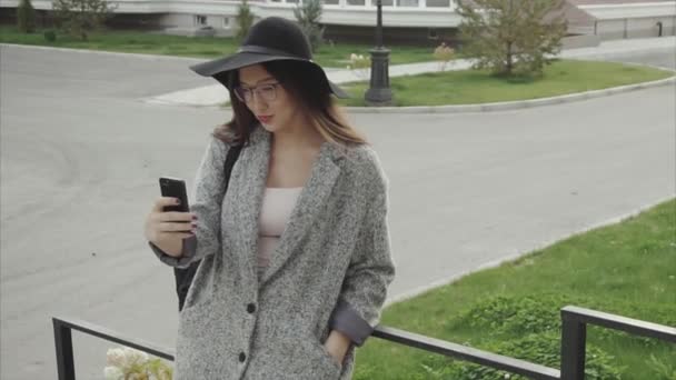 Bella donna in cappello nero e occhiali sms su smartphone all'aperto — Video Stock