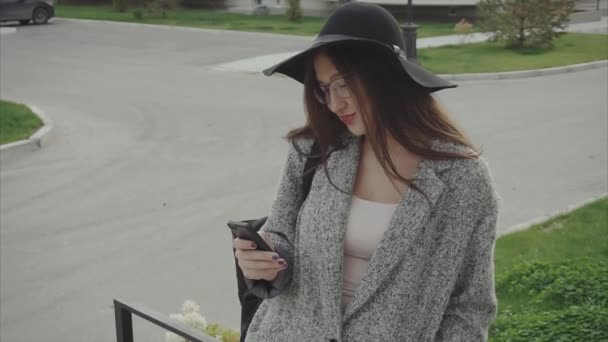 Elegante mooie vrouw in hoed en bril texting op smartphone in de stad — Stockvideo