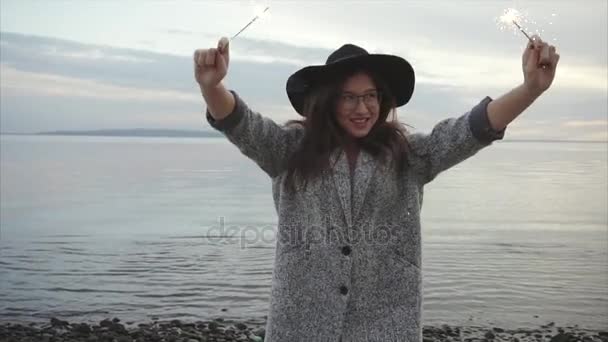 Красива жінка стрибає і радіє з блискавками на морському узбережжі на заході сонця — стокове відео