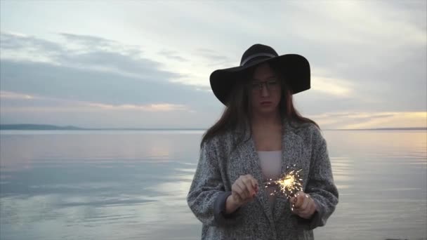 Mujer bastante feliz luces chispas en la costa del mar al atardecer — Vídeos de Stock