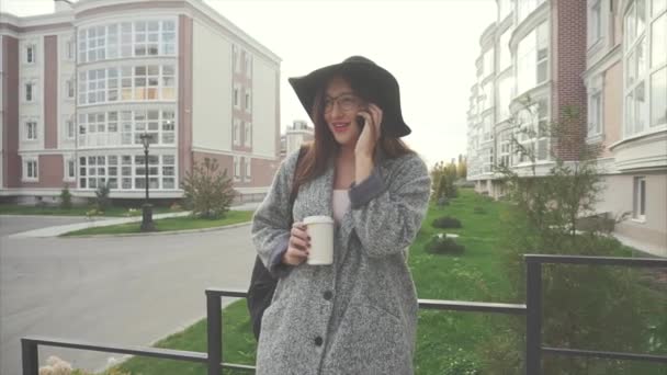 Kobieta w czarny kapelusz i okulary rozmowy na telefon komórkowy zewnątrz — Wideo stockowe