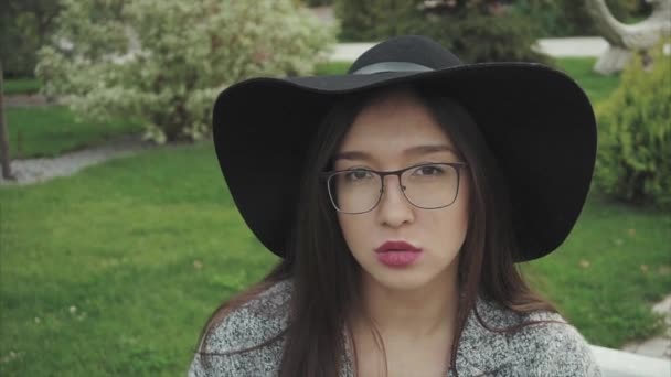 Närbild porträtt av allvarlig och eftertänksam kvinna i svart hatt och glasögon utomhus — Stockvideo