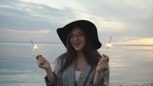 Ziemlich glückliche Frau jubelt mit Wunderkerzen an der Küste bei Sonnenuntergang — Stockvideo