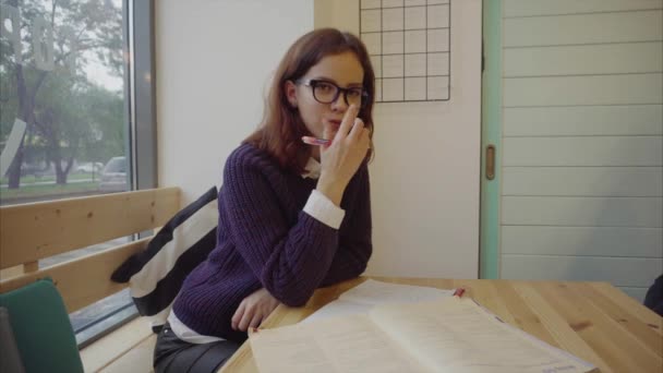 Bonita estudiante en gafas estudiando en la mesa con libros — Vídeos de Stock