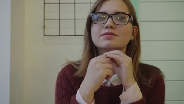 Close-up de jovem morena de óculos olhando para a câmera dentro de casa — Vídeo de Stock
