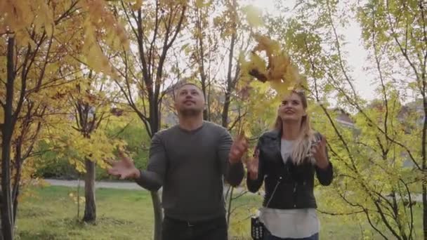 Jonge gelukkige paar spelen en gooien bladeren in de herfst park — Stockvideo