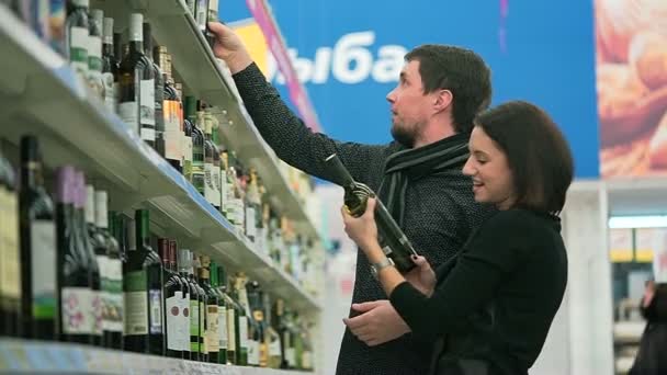 Jovem mulher e seu namorado escolhe uma garrafa de vinho . — Vídeo de Stock