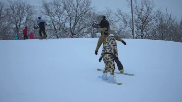 VOLZHSKII, RUSIA - 8 DE ENERO DE 2017: Una niña en una estación de esquí en el traje especial rodó en su tabla de snowboard, al pasar por otros snowboarders . — Vídeos de Stock