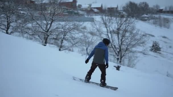 Joven activo deslizándose en una tabla de snowboard por la pendiente a alta velocidad . — Vídeos de Stock