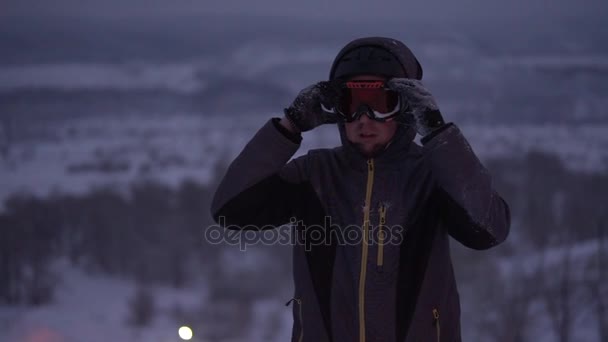 Joven se ajusta las gafas para esquiar por la noche en las pistas . — Vídeos de Stock