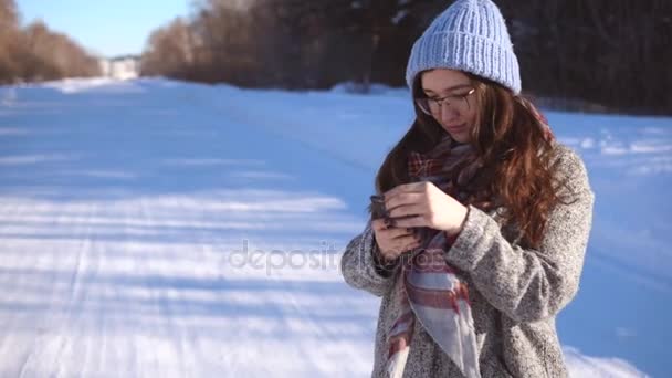 Menina na floresta de inverno perto da estrada lendo notícias em seu telefone celular . — Vídeo de Stock