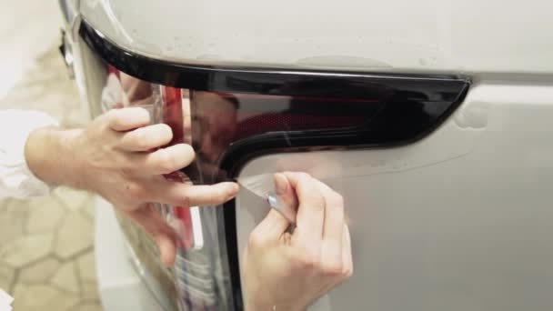 Close up shot of the hands of a man who peels the film from a white car. — Stock Video
