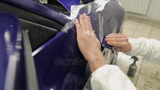 Primer plano plano de mans manos en la estación de servicio pegar vinilo en coche azul . — Vídeos de Stock