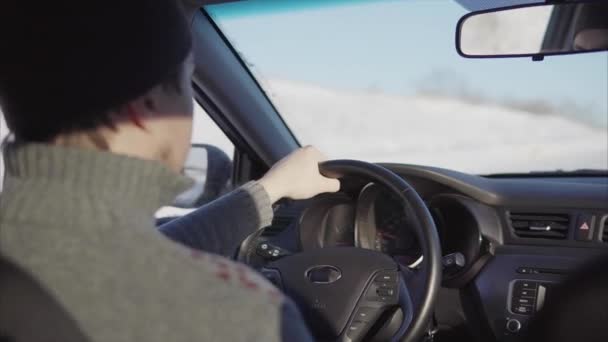 El joven conduce lentamente un coche en una carretera de invierno. . — Vídeo de stock